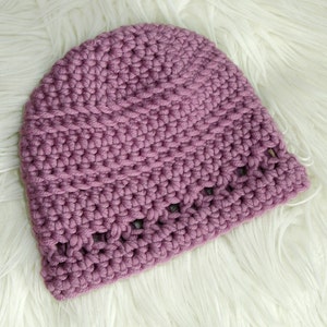 May include: A purple crocheted beanie hat with a textured stitch pattern and a decorative openwork border.
