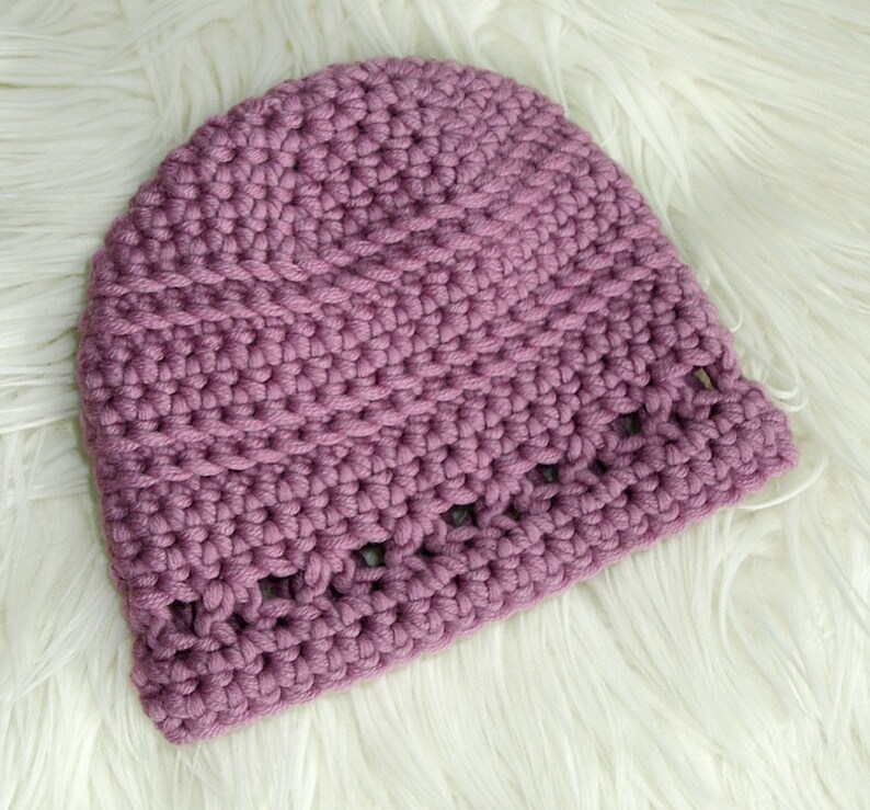 May include: A purple crocheted beanie hat with a textured stitch pattern and a decorative openwork border.