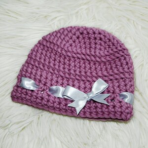 May include: A mauve crocheted hat with a silver satin ribbon bow.