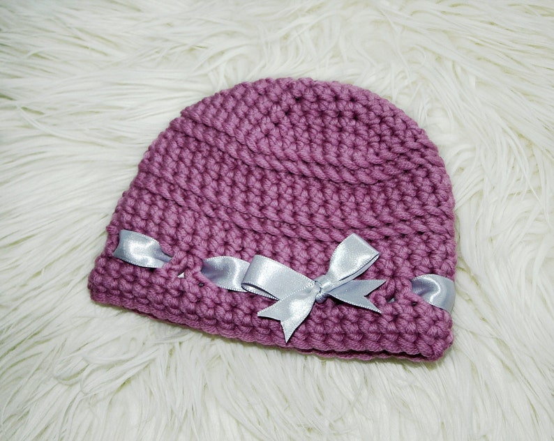 May include: A mauve crocheted hat with a silver satin ribbon bow.