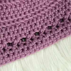May include: Close-up of a purple crocheted hat with a textured stitch pattern. The hat has a wide brim and is made with a thick yarn.