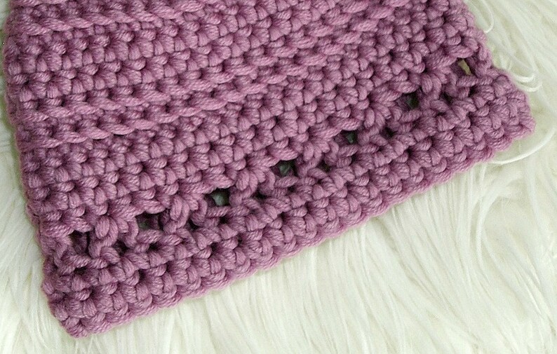 May include: Close-up of a purple crocheted hat with a textured stitch pattern. The hat has a wide brim and is made with a thick yarn.