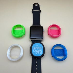 May include: An Apple Watch with a black band and several colorful protective cases. The cases are in green, pink, blue, and white. A blue and black band cover has the text "The Happiest Place on Earth".