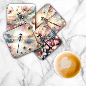 May include: Set of four square coasters featuring watercolor dragonfly designs with floral backgrounds. The dragonflies have iridescent wings in shades of blue, green, and pink. The coasters are on a marble surface, with a cup of coffee with a heart design.