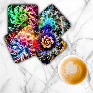 May include: Set of four square coasters with vibrant, abstract floral designs in shades of green, blue, red, and yellow. A cup of coffee with a heart-shaped foam design sits on a white marble surface.