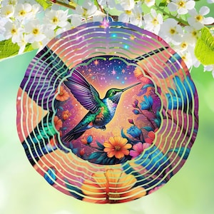 May include: A colorful metal wind spinner featuring a hummingbird with purple wings, green head, and a long black beak. The hummingbird is surrounded by flowers in shades of orange, blue, and pink. The background is a gradient of colors.