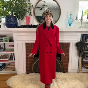 May include: A long, bright red coat with a black collar and black buttons. The coat is worn with a leopard print hat and brown boots. The coat is a classic style, suitable for cold weather.