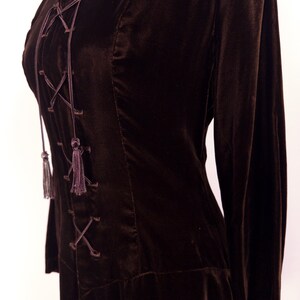 May include: A dark brown velvet top with long sleeves and a lace-up front. The top features a V-neckline and decorative tassels at the end of the lacing. The fabric has a soft, luxurious appearance.