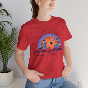 May include: Red t-shirt with a graphic print of a hibiscus flower and the text "The unexamined life is not worth living - Socrates".