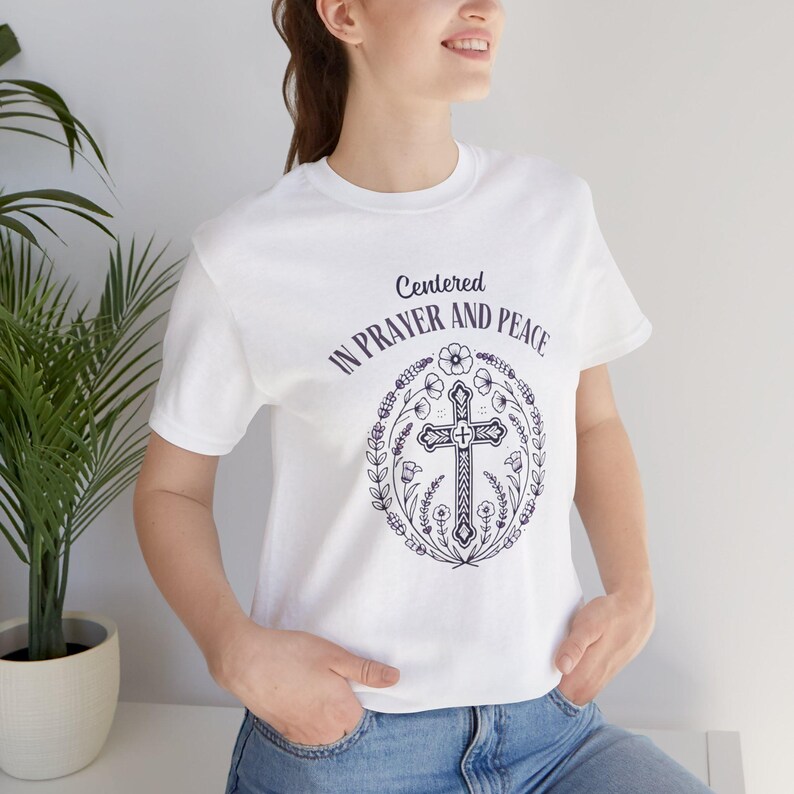 May include: White t-shirt with a graphic of a cross surrounded by flowers and the text "Centered in Prayer and Peace".