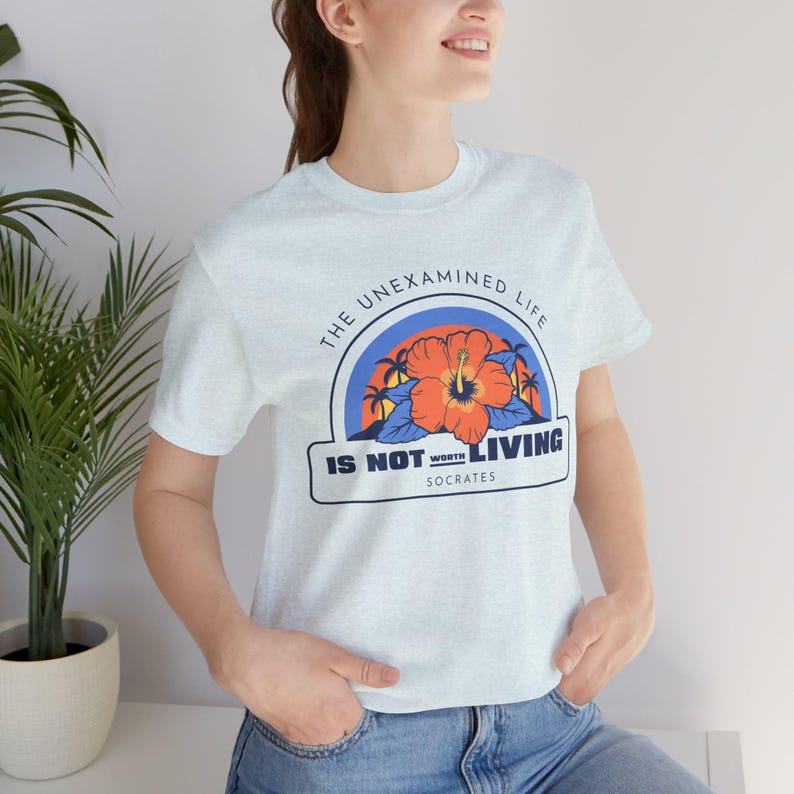 May include: Light blue t-shirt with a graphic print of a red hibiscus flower and palm trees. The text "The unexamined life is not worth living - Socrates" is printed on the shirt.