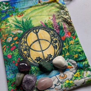May include: A green drawstring bag with a colourful floral print and a Celtic knot design. The bag contains six smooth, polished stones in various colours, including purple, green, white, and pink.