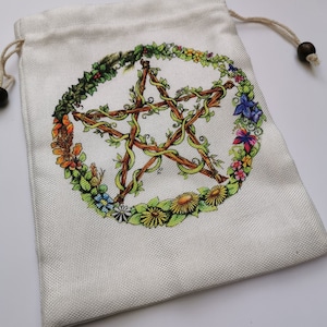 May include: A white drawstring bag featuring a pentagram design. The pentagram is crafted from brown twigs and encircled by a wreath of green leaves and vibrant flowers.