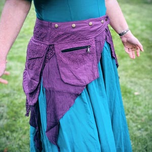 May include: A purple and teal skirt with a matching purple hip belt. The hip belt features a pocket with a zip and decorative buttons. The skirt is teal and has a flowing design.