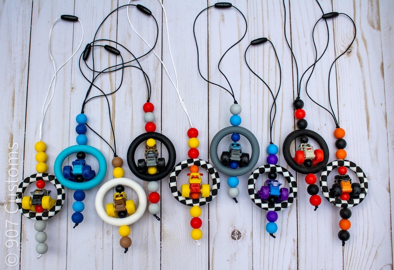 K&ouml;nnte beinhalten: Eine Sammlung von Schnullerhaltern f&uuml;r Babys mit Rennwagen-Designs. Jeder Halter hat eine farbenfrohe Perlenkette, einen Silikonring und ein kleines Spielzeug-Rennauto. Die Halter sind in verschiedenen Farben erh&auml;ltlich.