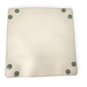 May include: A square, off-white leather tray with rounded corners and green circular accents at each corner. The tray has a stitched border with a light green thread. The tray is empty and sits on a white surface.