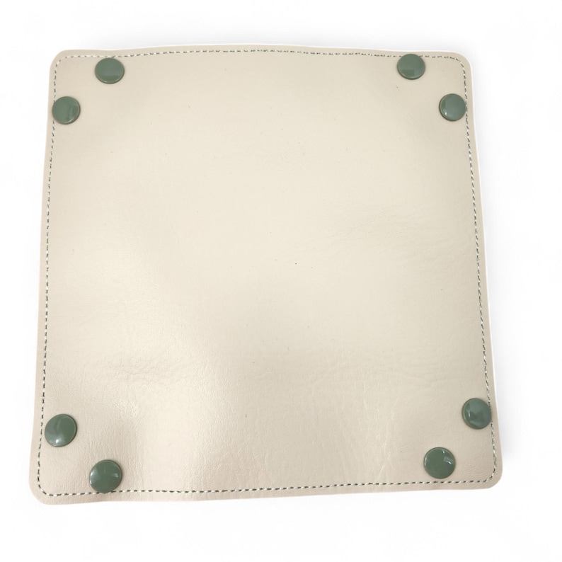 May include: A square, off-white leather tray with rounded corners and green circular accents at each corner. The tray has a stitched border with a light green thread. The tray is empty and sits on a white surface.