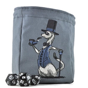May include: A gray fabric drawstring pouch featuring an embroidered meerkat wearing a blue vest, a black top hat, and a bow tie, while holding a blue pipe and a black cane. Three black twenty-sided dice with white numbers sit in front of the pouch.