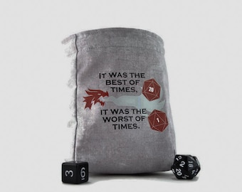 Puede incluir: Una bolsa de dados gris con el texto "IT WAS THE BEST OF TIMES, IT WAS THE WORST OF TIMES." Un gráfico de dragón rojo está encima del texto. Dos dados poliédricos rojos y un dado negro están al lado de la bolsa.