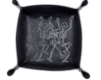 May include: Black leather tray with a white embroidered design of four skeletons dancing.
