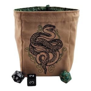 May include: Tan canvas dice bag with a black embroidered snake design and green accents. The bag has a green patterned interior and a drawstring closure. Three dice are in front of the bag, including a black D20, a black D6, and a green D20.