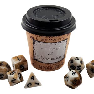 Puede incluir: Una taza de café marrón y blanca con una tapa negra. La taza tiene un diseño vintage con el texto "Espresso - 1 Level of Exhaustion Cappuccino Americano". Hay siete dados marrones y blancos esparcidos alrededor de la taza.