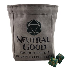 May include: A gray canvas dice bag with the words "Neutral Good" and "You don't need a reason to help people" printed in black. Two green and gold dice are next to the bag. The bag has a drawstring closure.