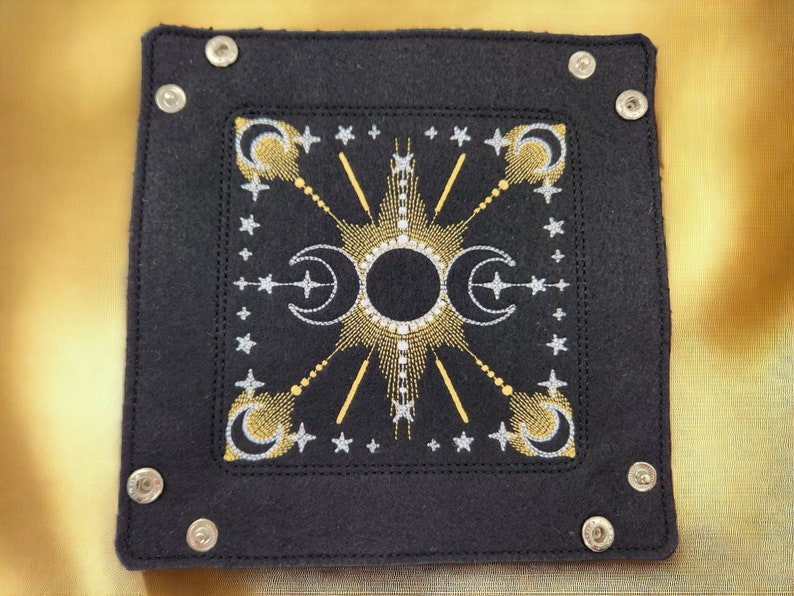 May include: Black felt tray with silver and gold embroidery of a sun and moon design. The tray has silver metal rivets around the edges.