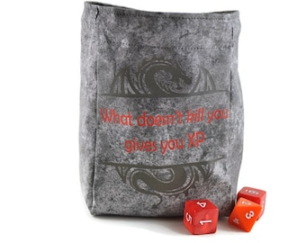 May include: Grey dice bag featuring a dragon design and the text "What doesn't kill you gives you XP." The bag is next to three dice, two red and one orange.