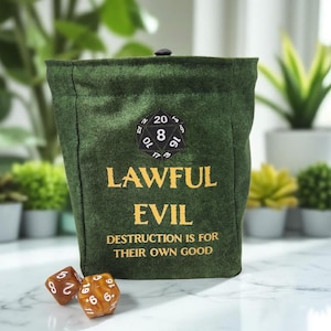 以下が含まれることがあります： 「LAWFUL EVIL」の文字が金色で書かれた、濃い緑色のサイコロバッグ。バッグには白黒のD20パッチと「DESTRUCTION IS FOR THEIR OWN GOOD」というフレーズがあります。バッグの前には2つのサイコロがあります。