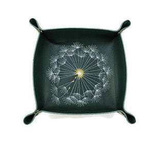 May include: A dark green leather tray with a white embroidered dandelion design. The tray has a square shape with rounded corners and a raised edge.