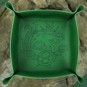 May include: A green leather dice tray with an embossed design of a turtle swimming in a pond with lily pads and reeds.