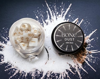 Puede incluir: Un pequeño frasco blanco con tapa negra que contiene dados blancos con números dorados. El frasco está etiquetado como "BONE DUST Mini dice".