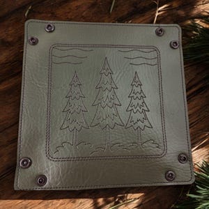 May include: A green leather tray with a stitched border and three trees embroidered in the center. The tray has metal rivets around the edges.
