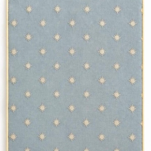 May include: A rectangular bulletin board featuring a light blue fabric surface with a repeating pattern of small, cream-colored embroidered starbursts. The board is framed by a thin, light-toned wooden border that surrounds the entire edge.