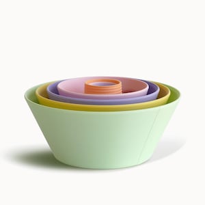 May include: A set of pastel-colored mixing bowls in shades of green, yellow, pink, purple, and orange. The bowls are nested inside each other, with the largest bowl in the front and the smallest in the center. The bowls are made of a smooth material.