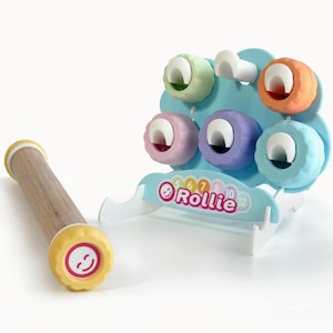 May include: A wooden toy with a yellow smiley face on one end and a light blue flower-shaped structure with colourful circular pieces. The structure has the word "Rollie" and numbers printed on it. The toy is designed for children.