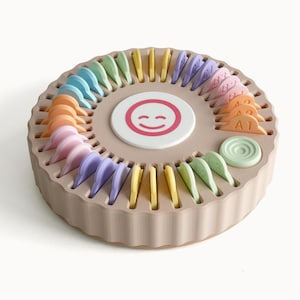 May include: A circular beige organizer tray with a scalloped edge, featuring a central white disc with a pink smiley face icon. The tray contains numerous pastel-colored dividers arranged in slots, with some labeled with alphanumeric codes like A1, A2, and B1.