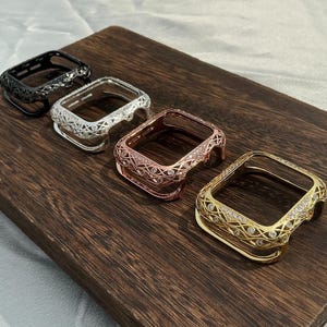 Pode incluir: Quatro capas protetoras retangulares para smartwatch nos acabamentos preto, prata, ouro rosa e dourado. Cada estrutura apresenta um intrincado padrão de treliça vazado, acentuado com pequenos cristais circulares transparentes.