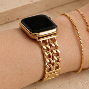 May include: A gold-toned smartwatch with a double-link chain strap and a black screen, accompanied by two thin gold-toned bracelets, one featuring a twisted design and the other a delicate chain with a small bead detail.