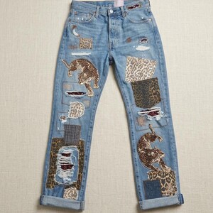May include: Light blue denim jeans with leopard print patches and distressed details. The jeans feature two leopard appliques and patches with distressed details. The jeans have a button fly and cuffed hems.