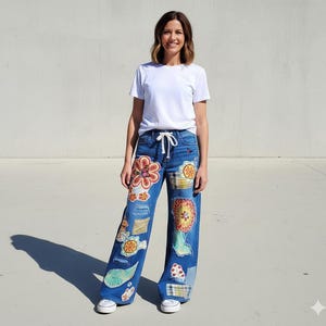 May include: Blue denim jeans with colorful floral and patchwork designs. The jeans have a wide leg and a drawstring waist. The person is wearing a white t-shirt and white sneakers.