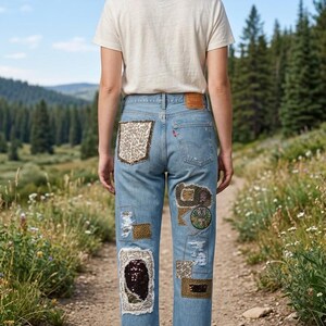 May include: Light blue denim jeans with decorative patches. The patches include leopard print, sequins, and embroidered designs. The jeans have a classic five-pocket design and a Levi's brand patch.