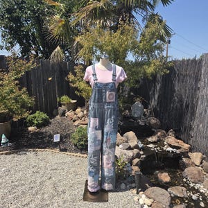 Könnte beinhalten: Eine blaue Jeanslatzhose mit einem Patchwork-Design aus verschiedenen blauen und hellrosa Stoffquadraten. Die Latzhose wird über einem einfarbigen, hellrosa T-Shirt mit kurzen Ärmeln getragen und ist auf einem Schaufensterpuppen-Torso präsentiert.