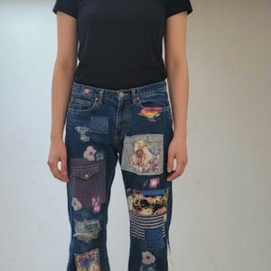 May include: Dark wash denim jeans with colourful patchwork designs. The jeans feature various floral and patterned patches, with a flared leg and frayed hem. A black t-shirt is worn with the jeans.