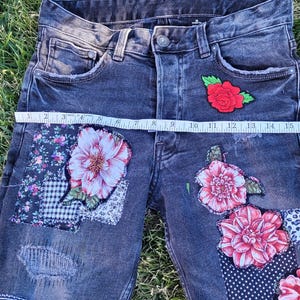 Könnte beinhalten: Dunkelblaue Jeansshorts mit floralen und Patchwork-Verzierungen. Die Shorts haben große Applikationen mit rosa Blumen, eine rote Rose und verschiedene Stoffflicken. Die Shorts werden mit einem Maßband gemessen.