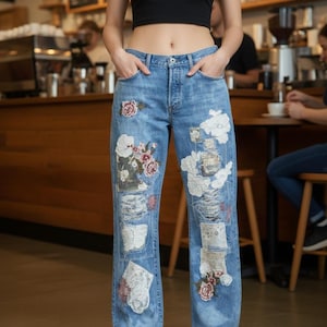 May include: Light blue denim jeans with floral and patchwork designs. The jeans have a high waist and a relaxed fit. The patches feature embroidered flowers and other decorative elements. The model is wearing a black crop top and black shoes.