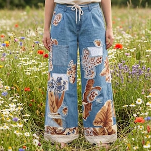 May include: Light blue denim pants with floral patchwork and a drawstring waist. The wide-leg pants feature patches of various floral designs in shades of brown, blue, and cream. The hemline is trimmed with lace.