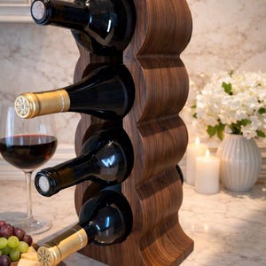 May include: A wooden wine rack holds four bottles of wine. The rack is made of dark wood and has a unique, curved design. A glass of red wine, cheese, and grapes are on the counter.
