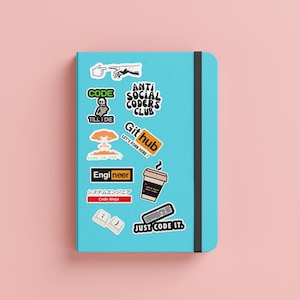 May include: A blue notebook with various stickers on it. The stickers feature text like "Code", "Anti Social Coders Club", "Git Hub", "Engineer", and "Just Code It".